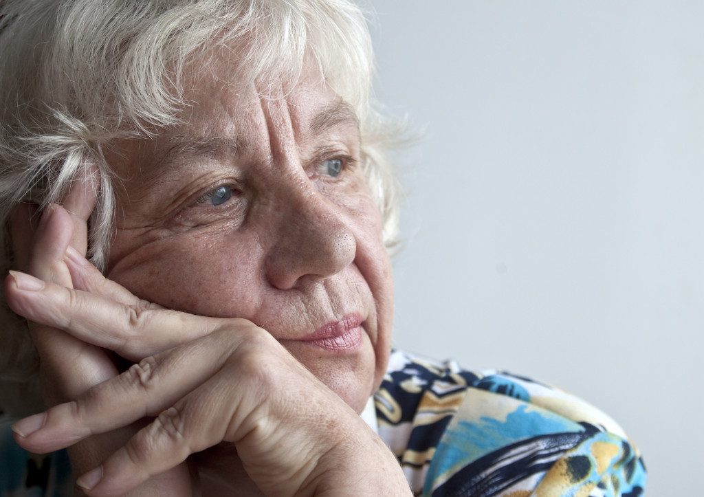 A sad elderly woman leaning on her hands and staring far away