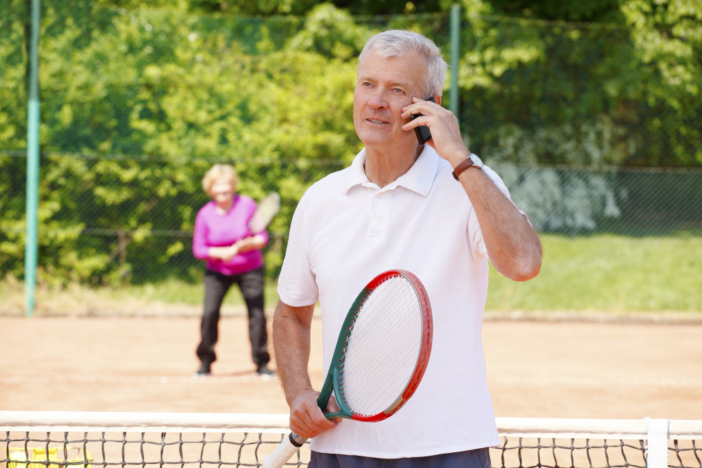 Old man talking on phone while playing tennis 