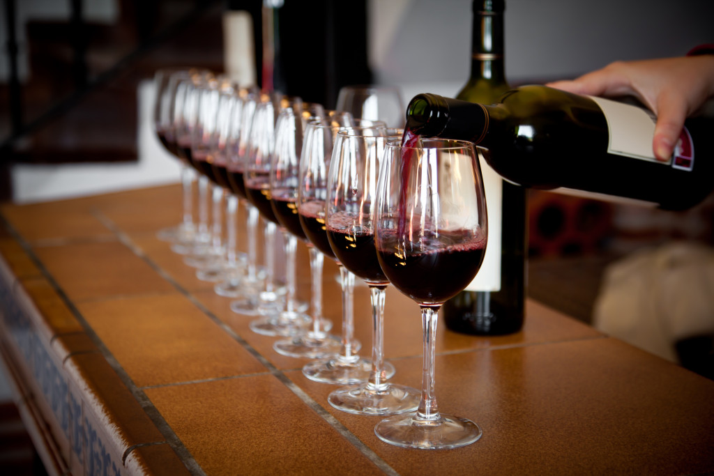 A hand pouring wine from a bottle on a line of wine glasses for tasting