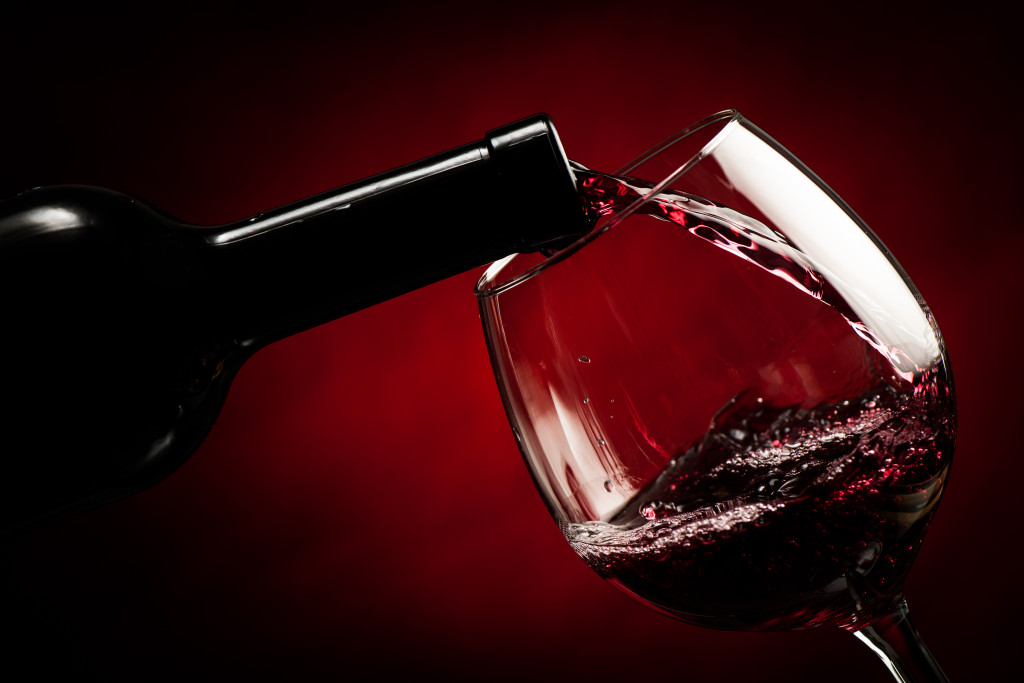 red wine being poured into a wine glass from a wine bottle in red background
