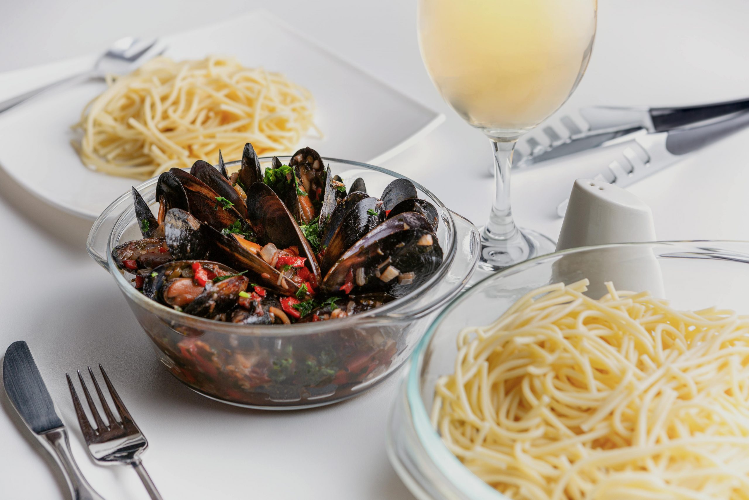 bowls of shellfish and pasta noodles, and a glass of white wine