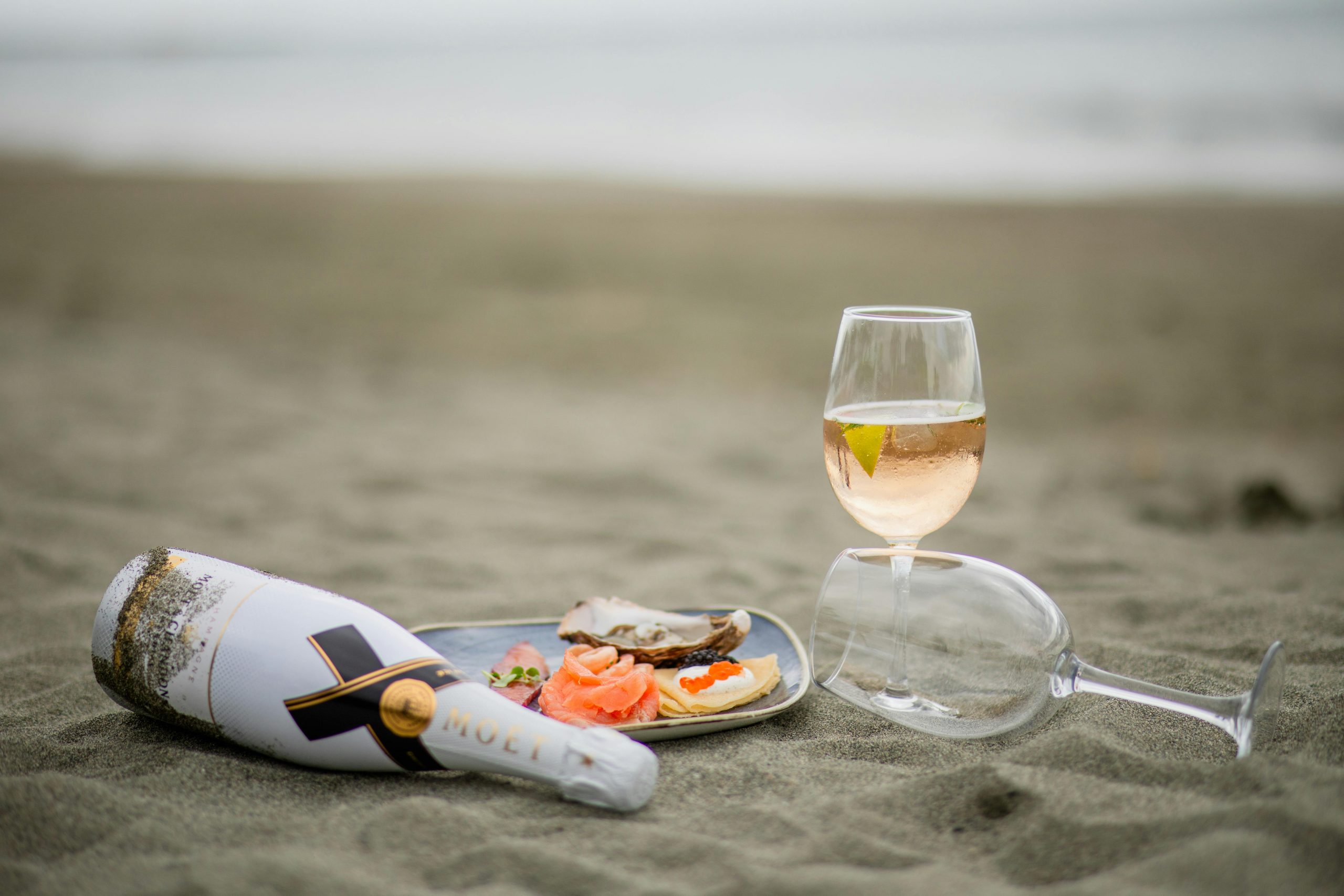 bottle and glasses of white wine with a seafood dish on the sand