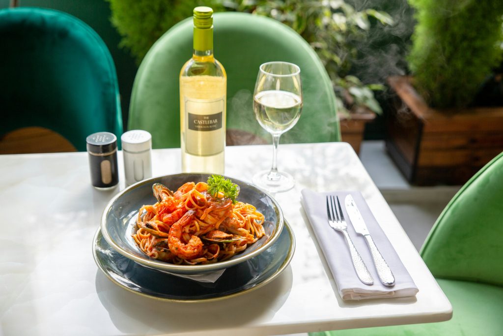 bottle and glass of white wine, and seafood pasta on a table